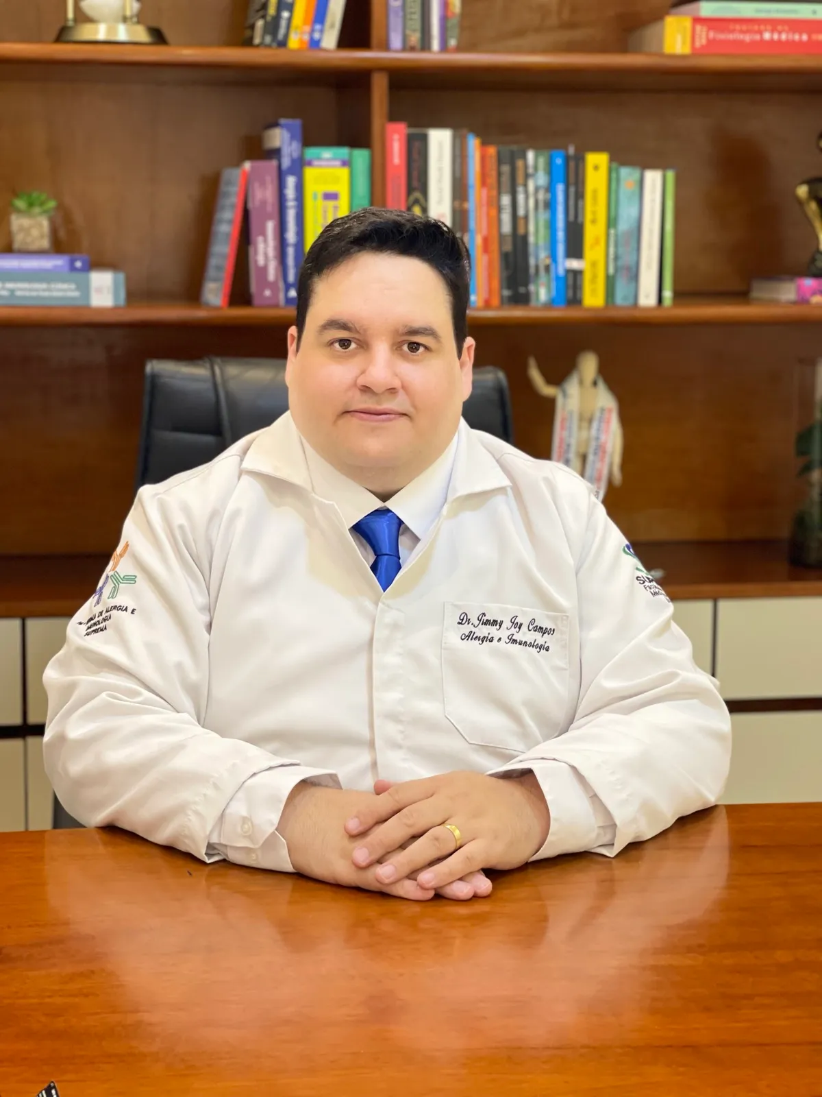 Dr. Jimmy Joy Campos, médico especialista em Clínica Médica, de jaleco em seu consultório